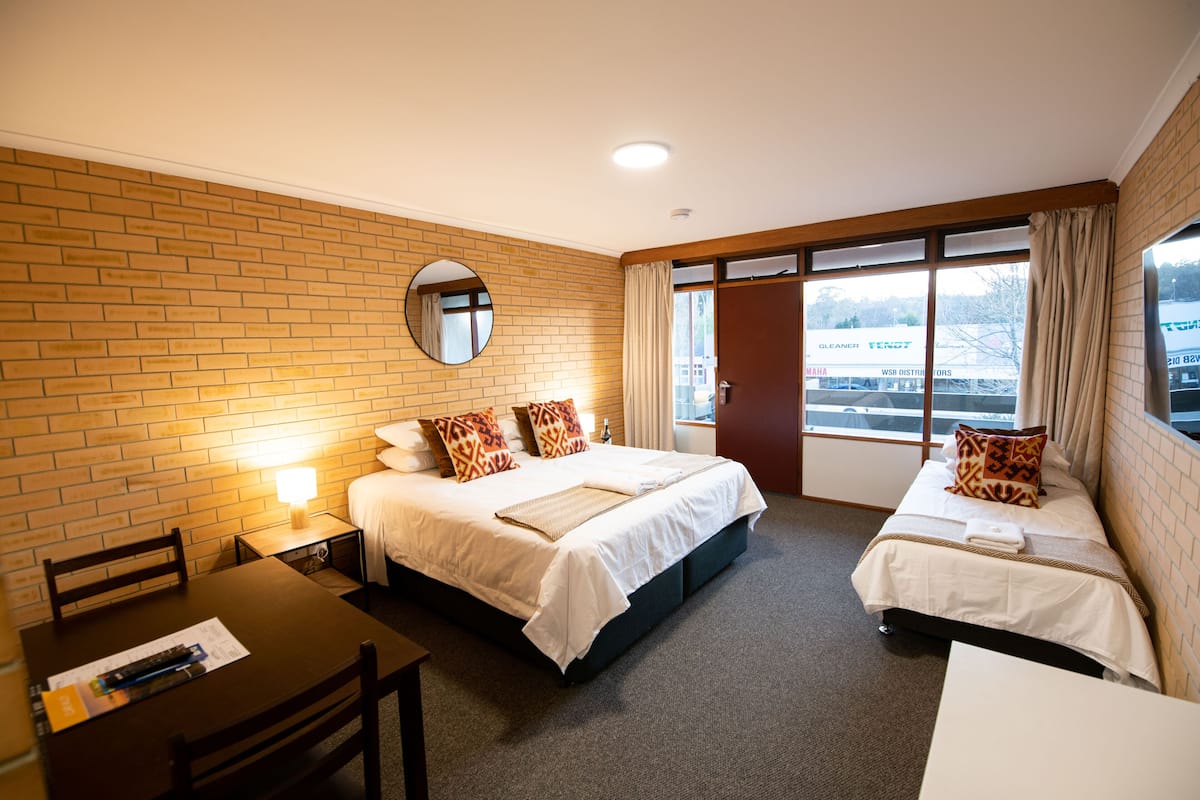 Habitación de hotel con dos camas, un escritorio, una silla, un espejo redondo y una ventana con cortinas.