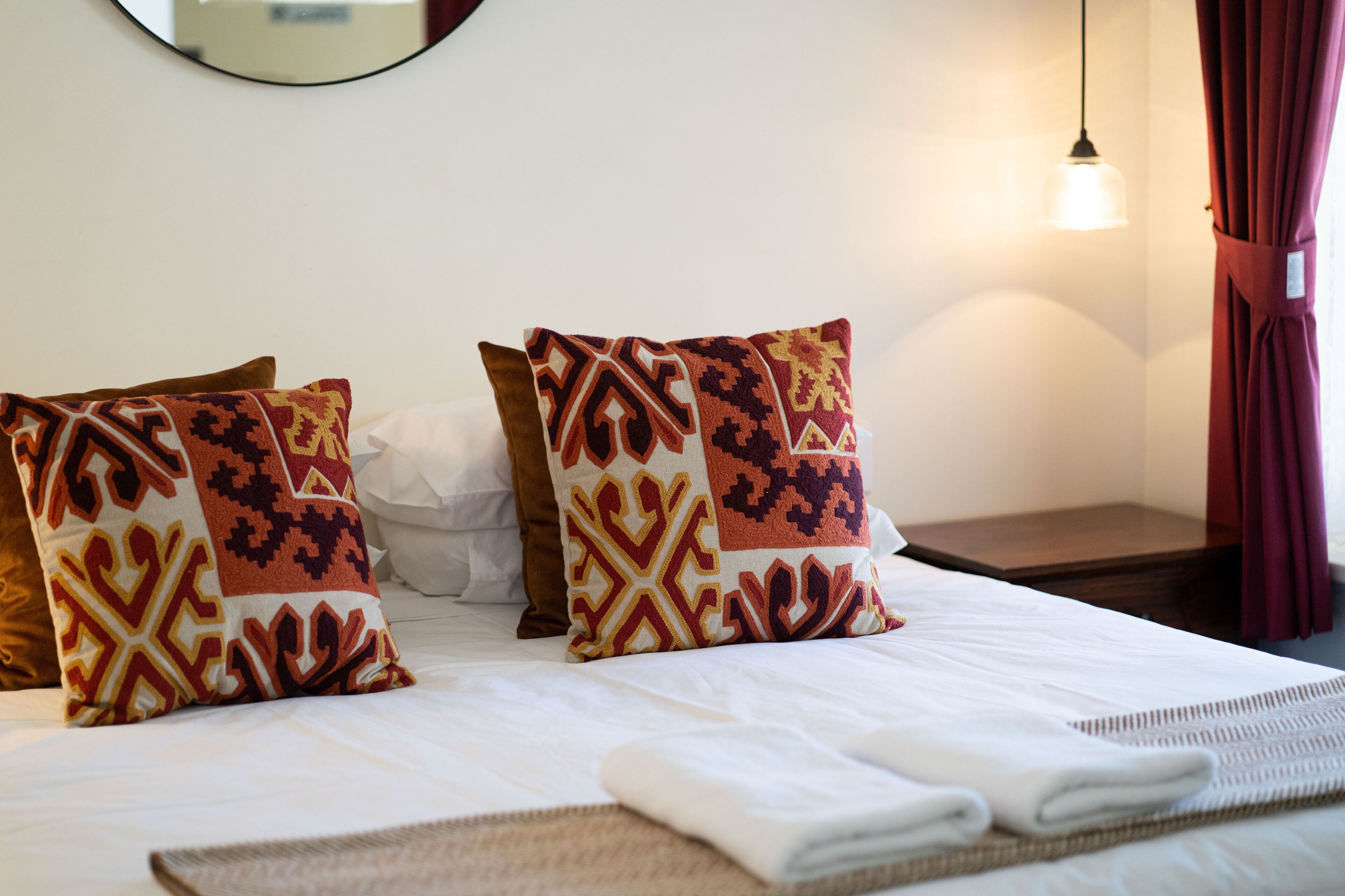 A neatly made bed with patterned pillows, a folded towel, and a small table.