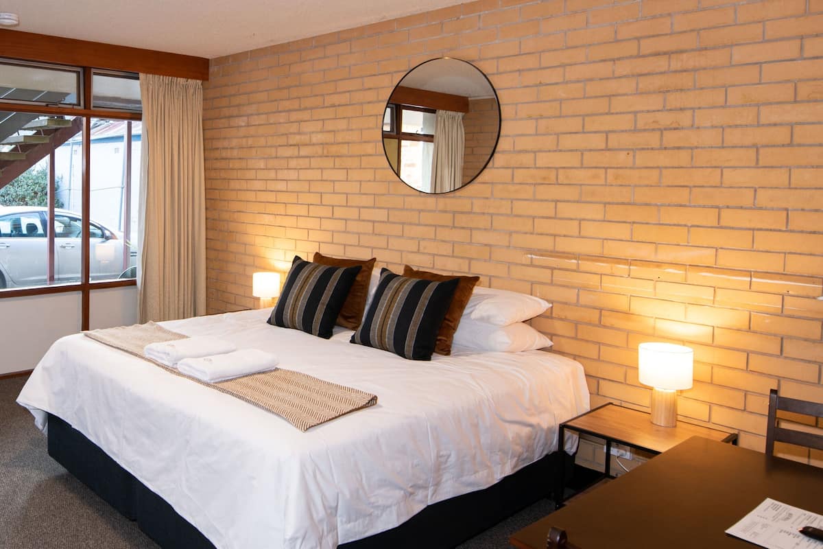 Habitación de hotel con pared de ladrillo, una cama grande con ropa blanca, almohadas a rayas, un espejo redondo y dos lámparas de noche.