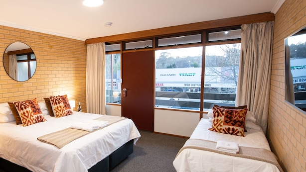 Une chambre d’hôtel avec deux lits, une grande fenêtre avec des rideaux, un mur en briques et un miroir.