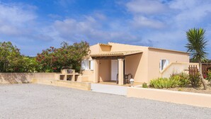 Une villa de couleur beige dotée d’un patio couvert, d’une porte et d’un petit jardin agrémenté de plantes et d’un palmier.