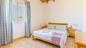 Une chambre à coucher avec un lit en bois, deux tables de chevet, une fenêtre avec des rideaux et un plancher carrelé.