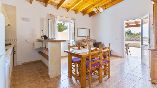 Une cuisine avec des poutres en bois, une table à manger avec des chaises, un comptoir en pierre et une vue par la fenêtre.
