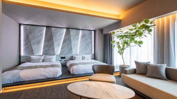 Una habitación de hotel moderna con una cama grande, un sofá, una mesa redonda y una planta en maceta.