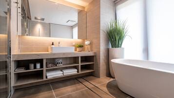 A modern bathroom with a large bathtub, a glass shower enclosure, a vanity with a mirror, and a potted plant.