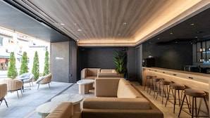 Un moderno hall de hotel con zona de estar, bar y un gran ventanal con vistas a la calle.