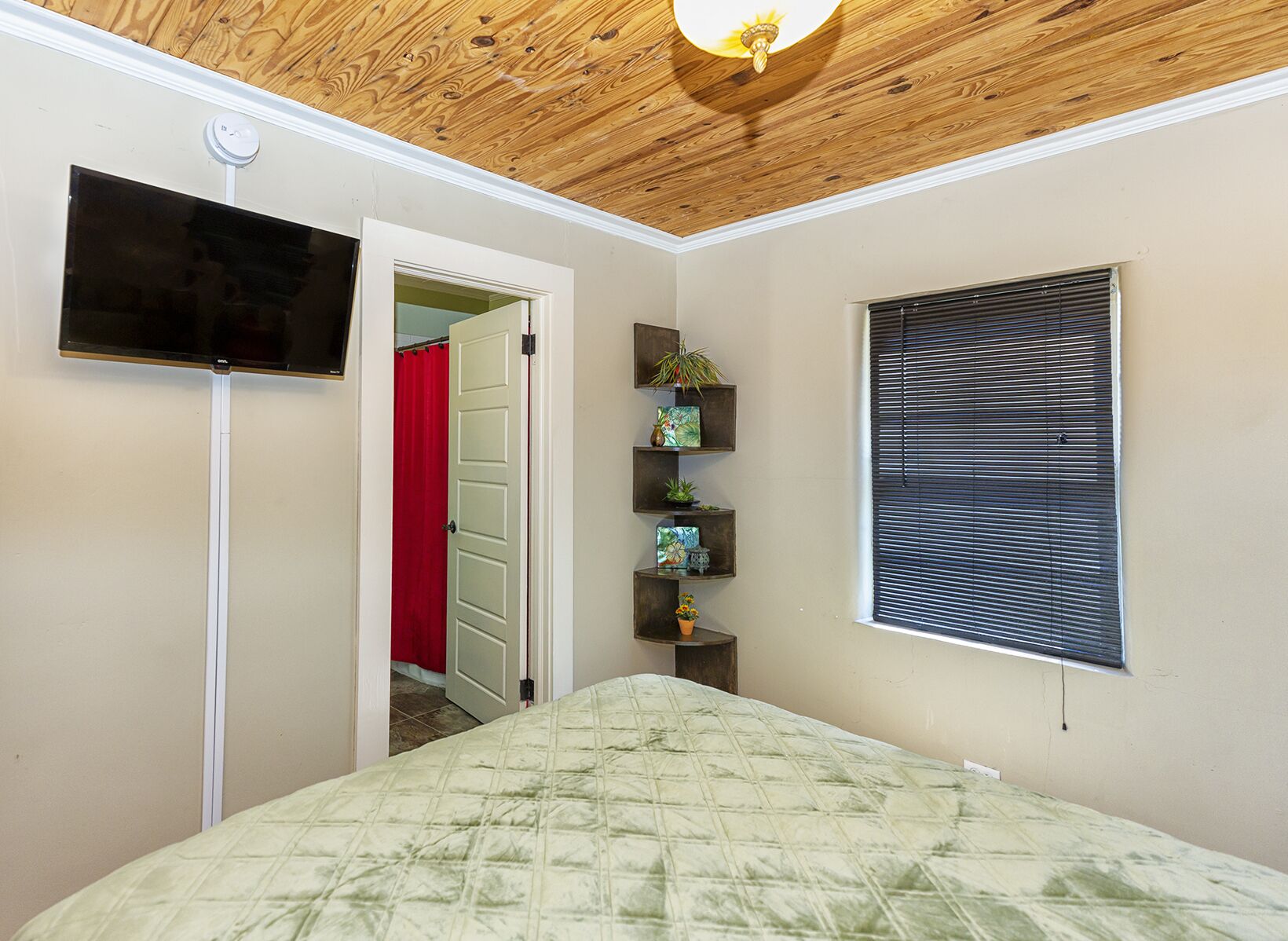 Een slaapkamer met een bed, een tv die aan de muur hangt, een plafondventilator en een raam met jaloezieën.