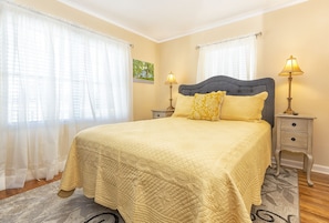 A bedroom with a large bed, two bedside tables with lamps, and sheer curtains.