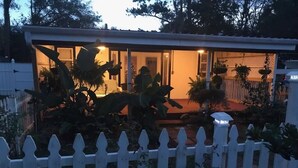 Una casa con valla de piquete blanca, un porche cubierto y varias plantas.