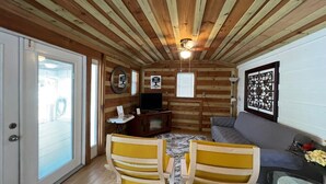 Interior acogedor de una cabaña con techo de madera, un sofá, dos sillones amarillos, un televisor y un elemento decorativo en la pared.