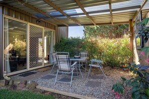 A covered patio with a table and chairs, surrounded by gravel and plants.
