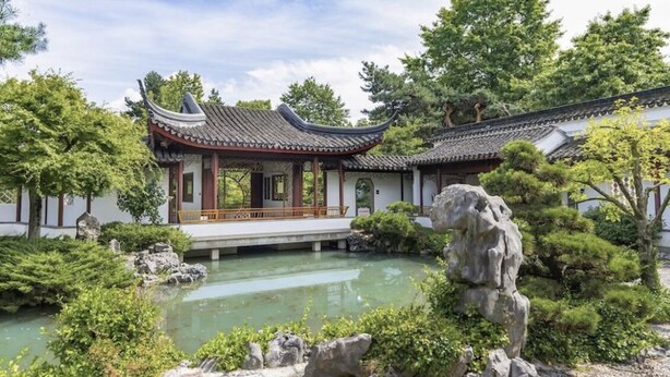 A traditional Chinese garden with a pavilion, a pond, and rock formations.