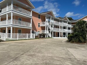 A multi-story hotel with balconies, a concrete driveway, and a clear sky.