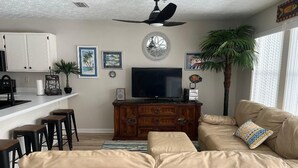A living room with a beige sectional sofa, a TV, a wooden cabinet, and a ceiling fan. - Panama City Beach West Side Gem — Steps to the Beach, Poolside, Ground‑Floor (Panama City Beach)