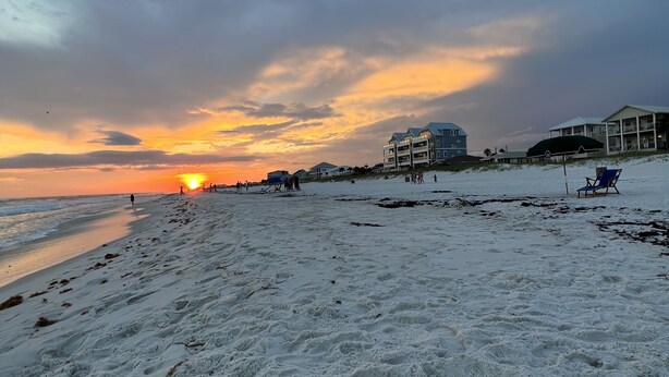 A beach with footprints, a sunset, and buildings in the background. - Panama City Beach West Side Gem — Steps to the Beach, Poolside, Ground‑Floor (Panama City Beach)