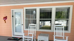 A porch with two rocking chairs and a small table, a door, and barred windows. - Panama City Beach West Side Gem — Steps to the Beach, Poolside, Ground‑Floor (Panama City Beach)