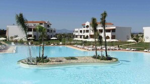 A large swimming pool with lounge chairs and umbrellas, surrounded by palm trees and buildings with balconies. - Italian Beach Resort Apartment (Via Carlo Enrico Bernasconi, Scanzano Jonico MT)