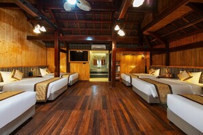 Une chambre d’hôtel avec quatre lits disposés de manière symétrique, un plancher en bois et un escalier central menant à un étage supérieur.