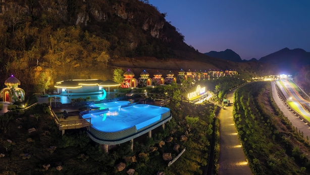 A resort with a swimming pool, multiple buildings with unique architecture, and a well-lit pathway. - Moc Chau Island - Mountain Park and Resort (Moc Chau)