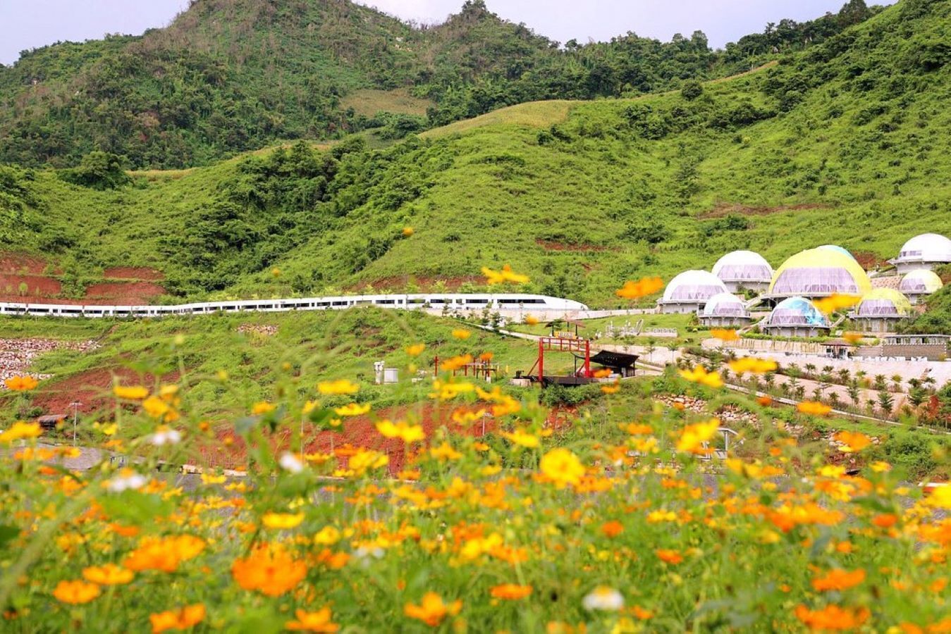 A train station with a white train, green hills, and dome-shaped buildings in the background.