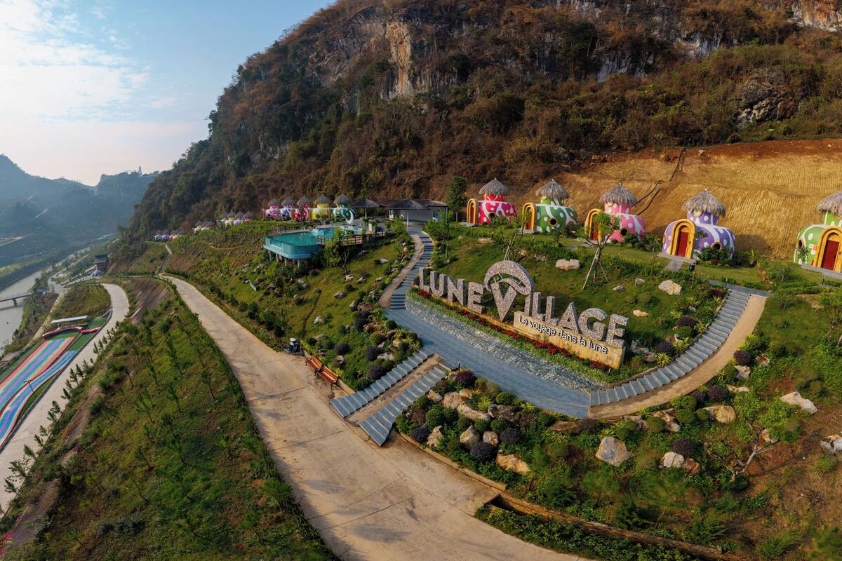A hillside village with colorful, uniquely designed huts, a winding road, and a river in the background.
