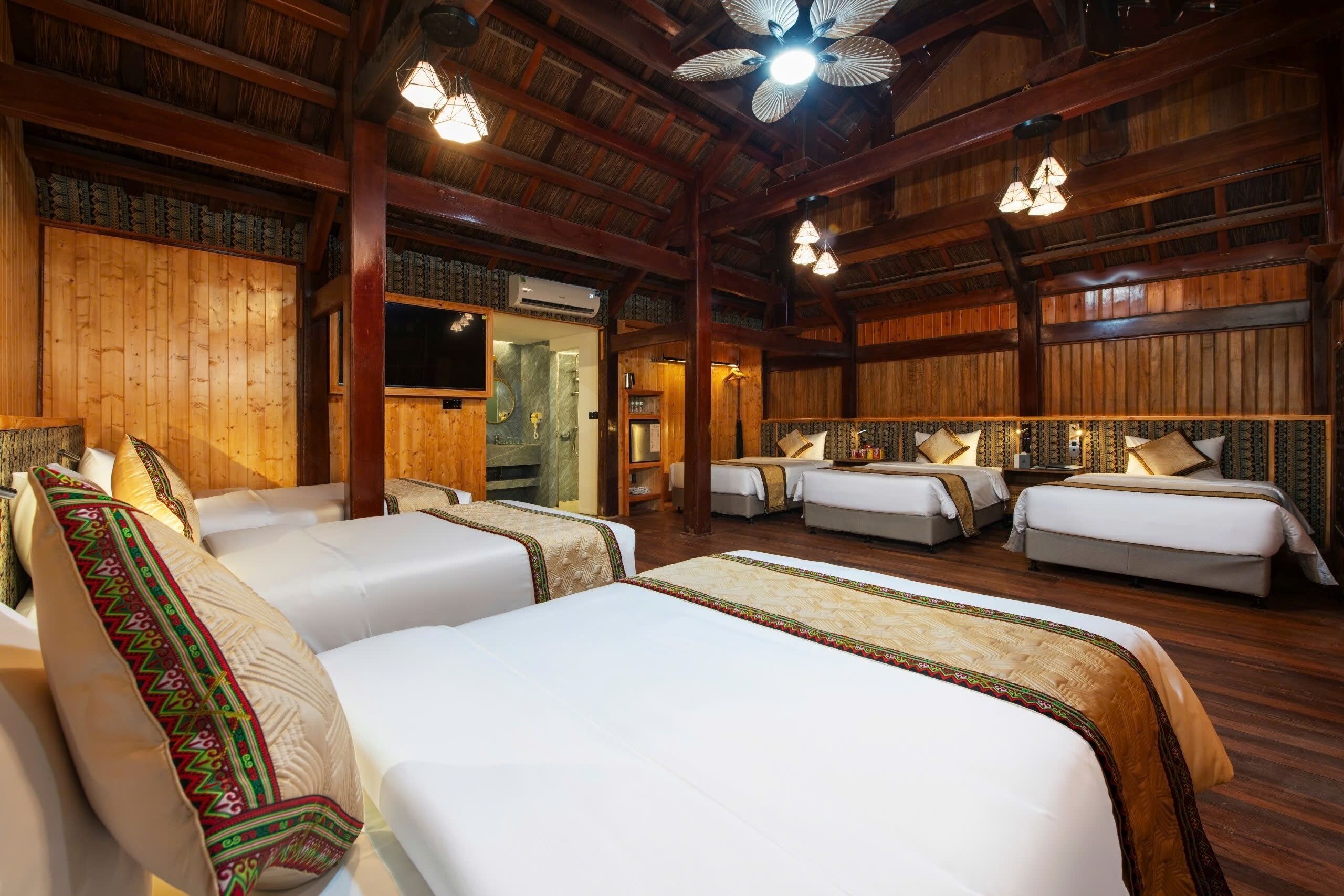 A hotel room with wooden walls, four beds, a ceiling fan, and a bathroom with a mirror.