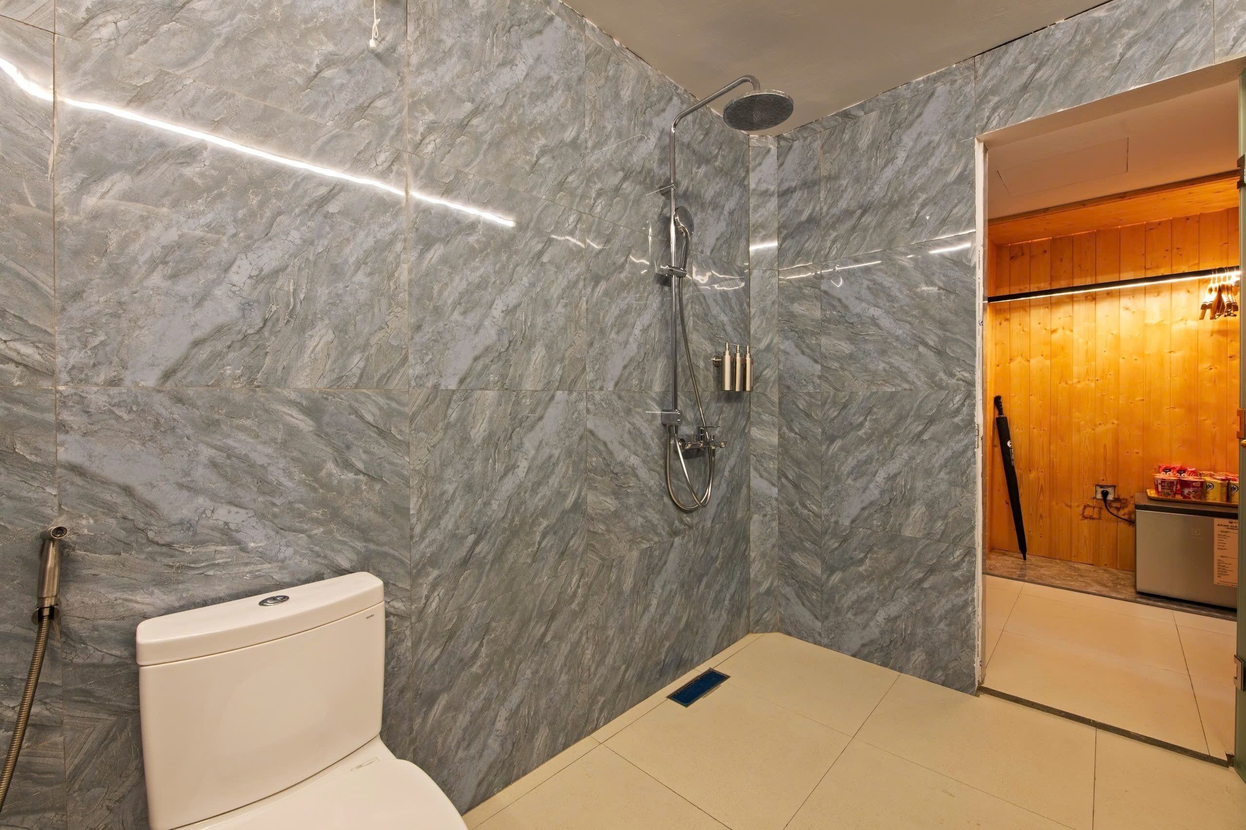 A bathroom with a marble wall, a shower, a toilet, and a wooden cabinet.