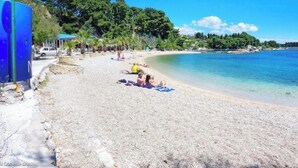 A beach with clear blue water, a few people sunbathing, and a blue lamp post. - Apt Sleeps 2 with Sea Proximity (Split)