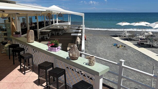 A beachside bar with outdoor seating, a view of the ocean, and a deck area with lounge chairs. - 1 Bed Cottage Sleeps 4 Private Garden - Pool (Colletta)