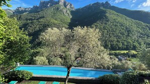 A pool area with a mountain backdrop, surrounded by lush greenery and a prominent tree. - 1 Bed Cottage Sleeps 4 Private Garden - Pool (Colletta)