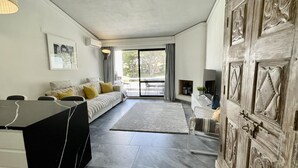 A modern living room with a sofa, a coffee table, and a TV. There is a large wooden cabinet and a sliding glass door leading to a balcony. - Scarlet's Place - Spacious 1 bed Quinta Do lago (Quinta do Lago)