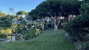 A well-maintained garden with a variety of trees, a small pond, and a clear sky. - Scarlet's Place - Spacious 1 bed Quinta Do lago (Quinta do Lago)