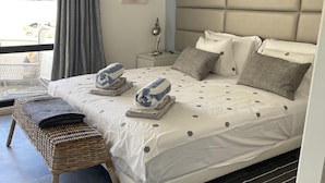 A bedroom with a large bed, a bedside table, a lamp, and a view of the outside. - Scarlet's Place - Spacious 1 bed Quinta Do lago (Quinta do Lago)