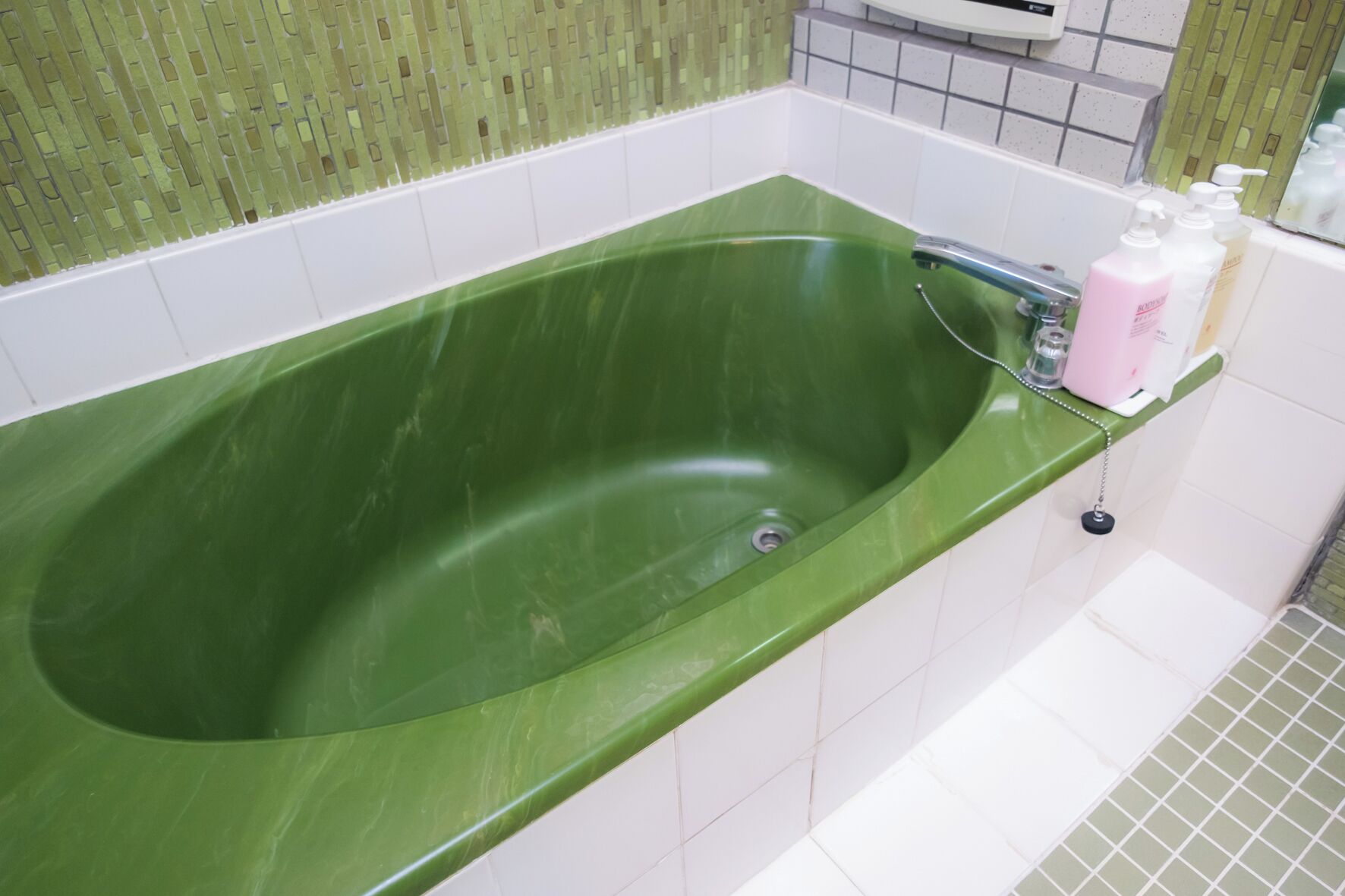 A green bathtub with a chrome faucet and a white tiled wall.