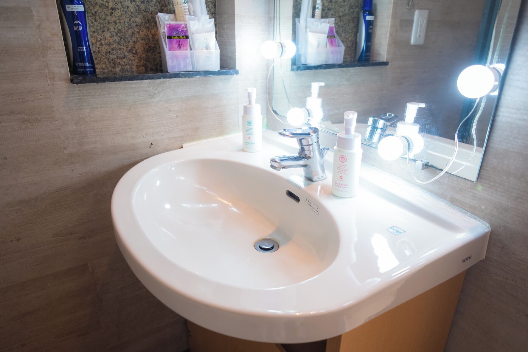 A bathroom with a white sink, a mirror, and toiletries on the countertop.