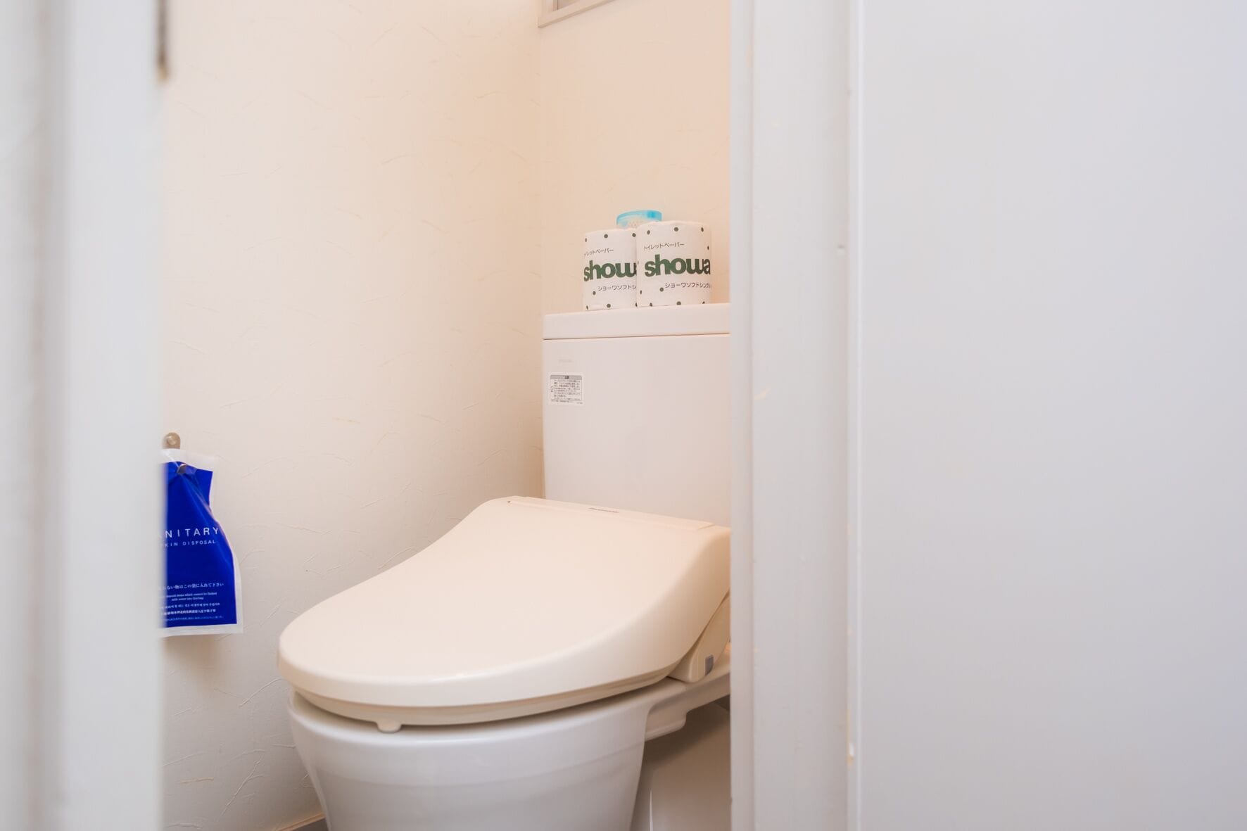 Un inodoro pequeño y blanco con la tapa bajada, una bolsa azul colgada en la pared y un letrero encima del inodoro.