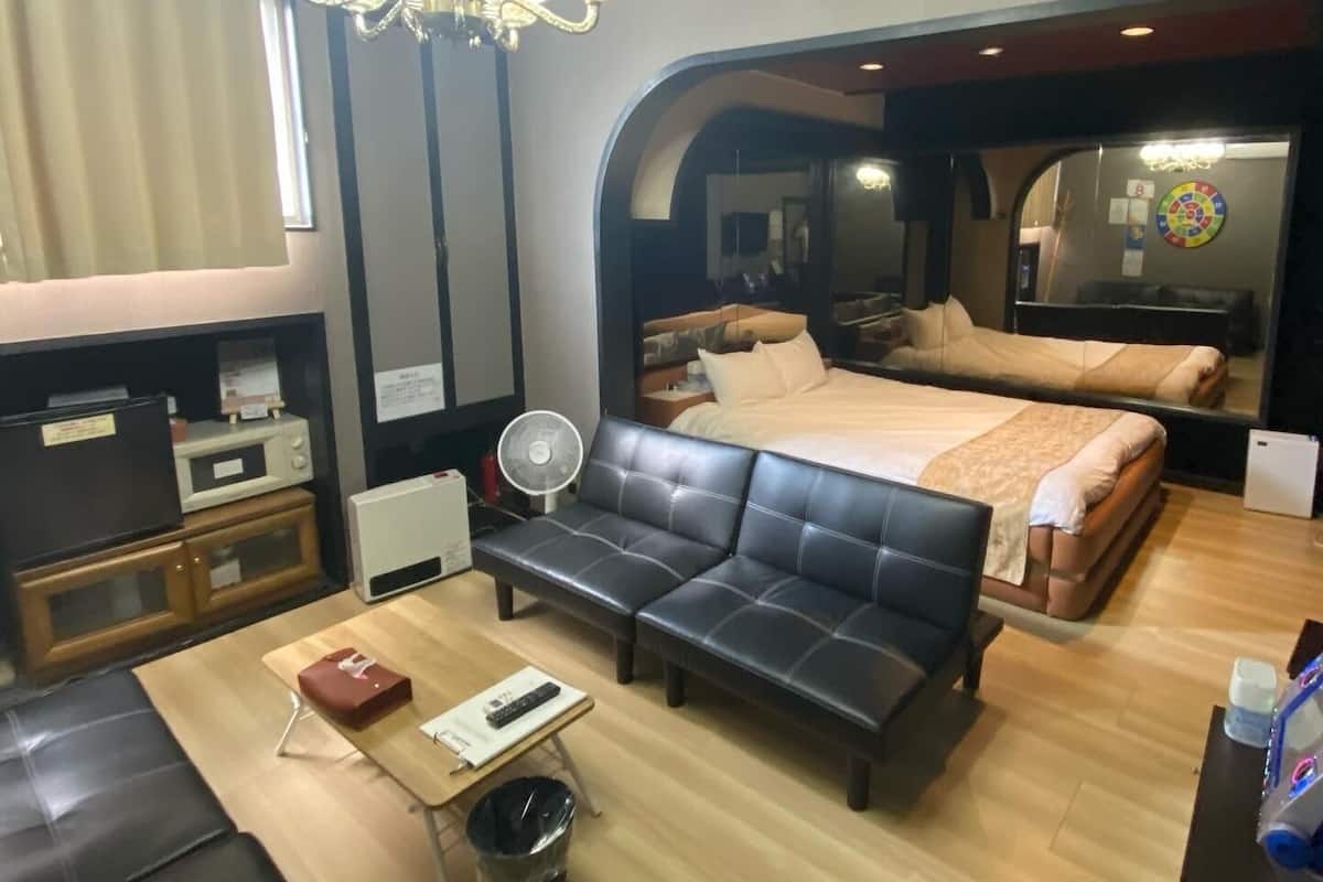 A modern hotel room with a large bed, a sofa, a desk, and a mirror.