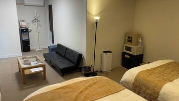 Habitación de hotel con dos camas, un sofá, una mesita, una lámpara, microondas y un cubo de basura.