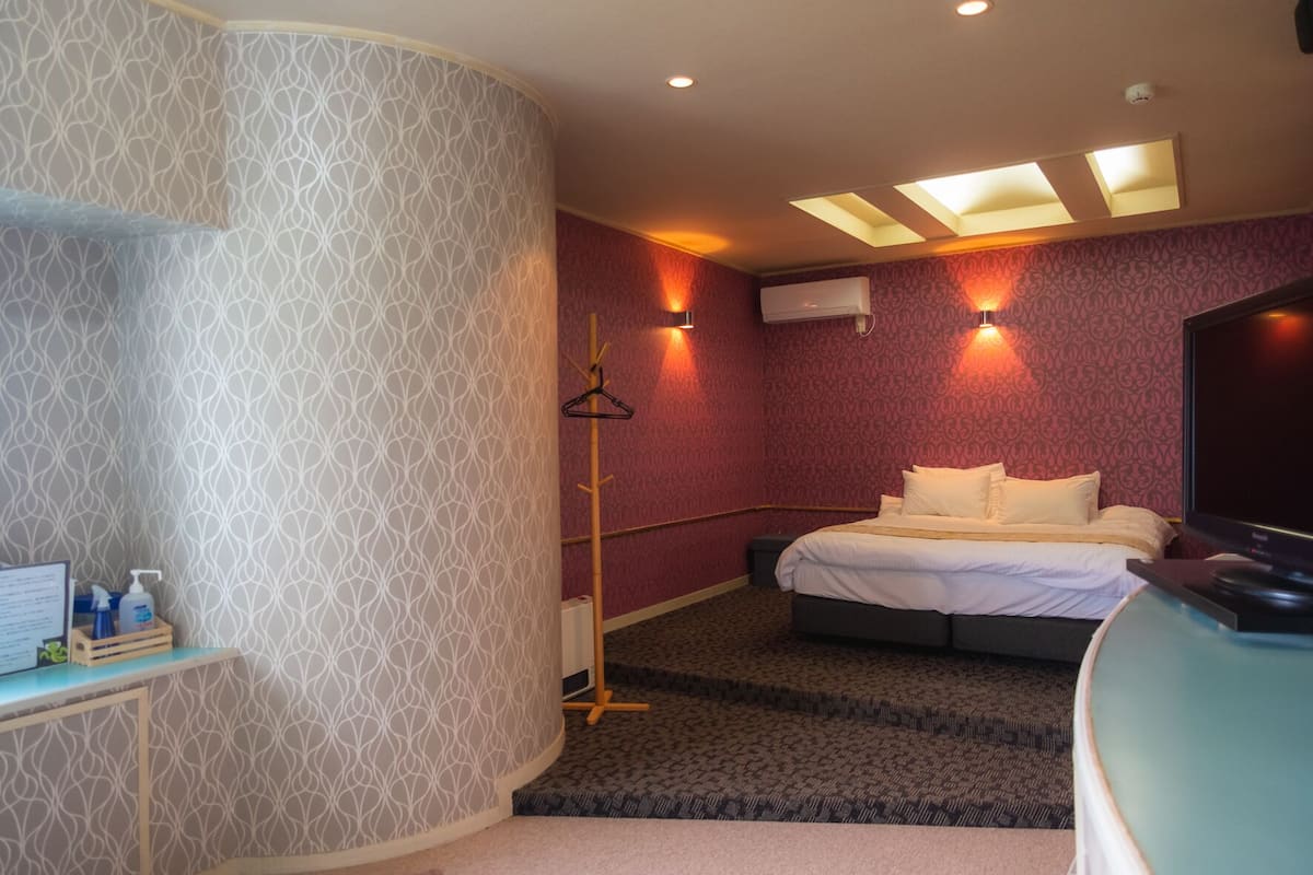 A hotel room with a bed, a TV, a coat rack, and a desk with toiletries.