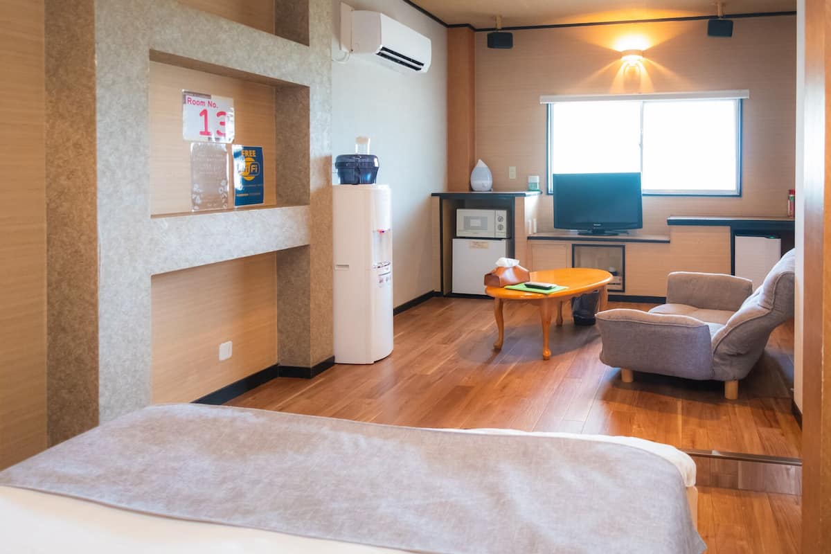 A compact hotel room with a bed, a small kitchenette, a TV, and a sofa.