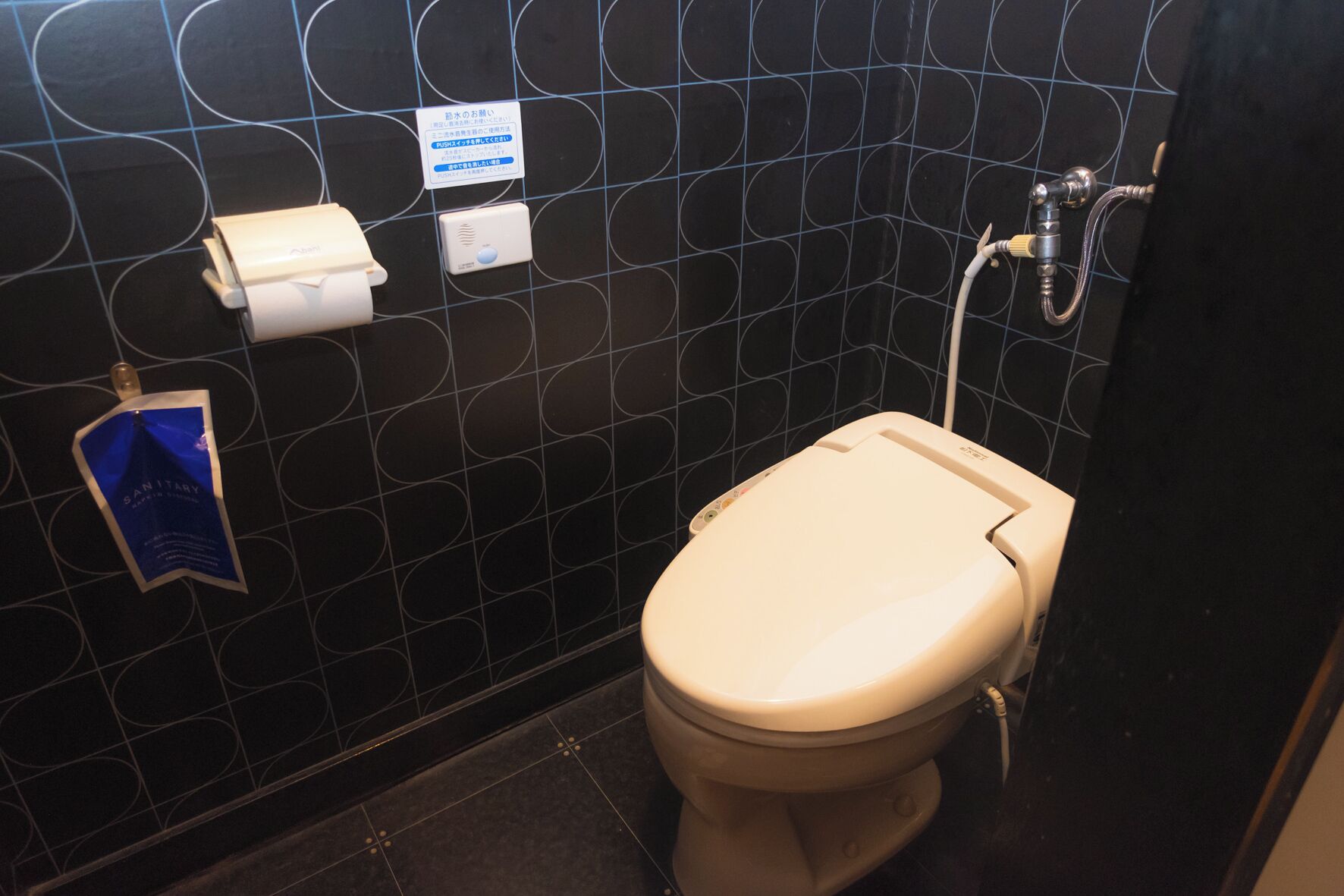 Un baño con inodoro, secamanos y dispensador de toallas de papel.