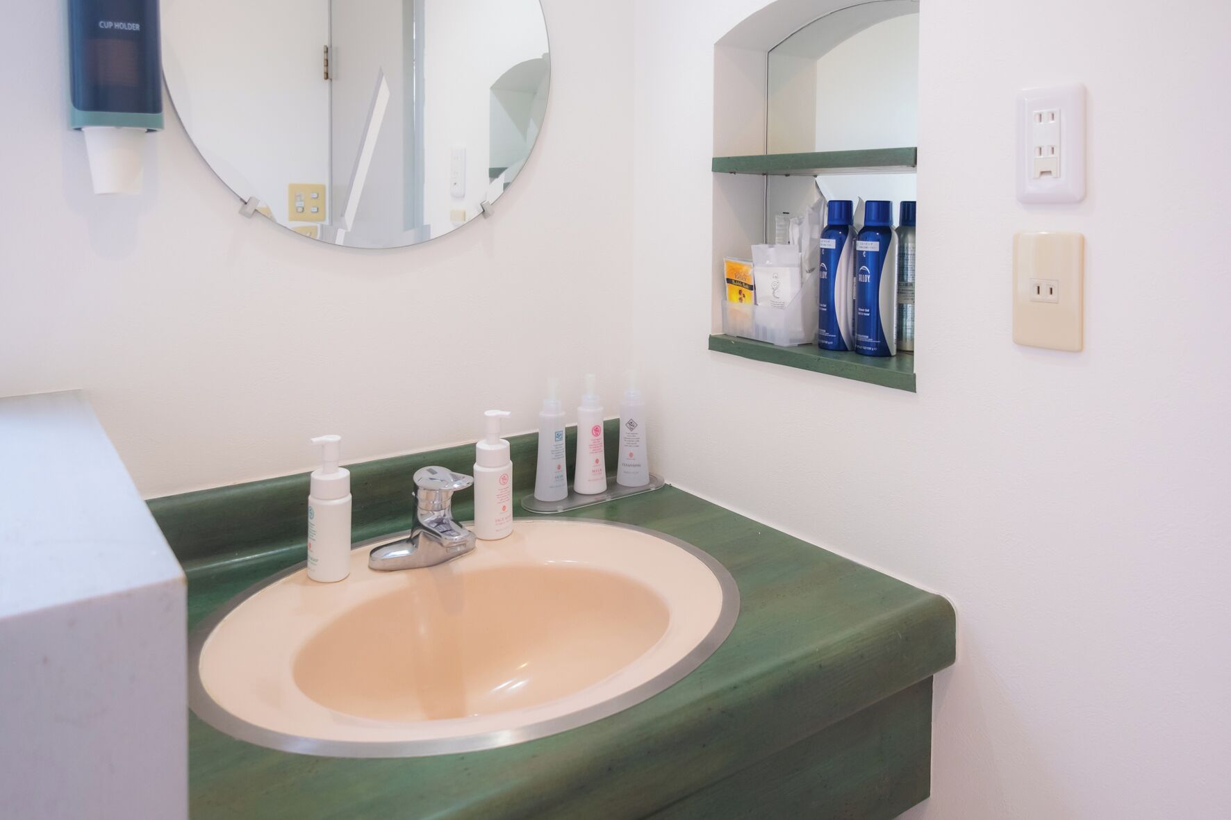 A bathroom with a sink, mirror, and toiletries on a shelf.