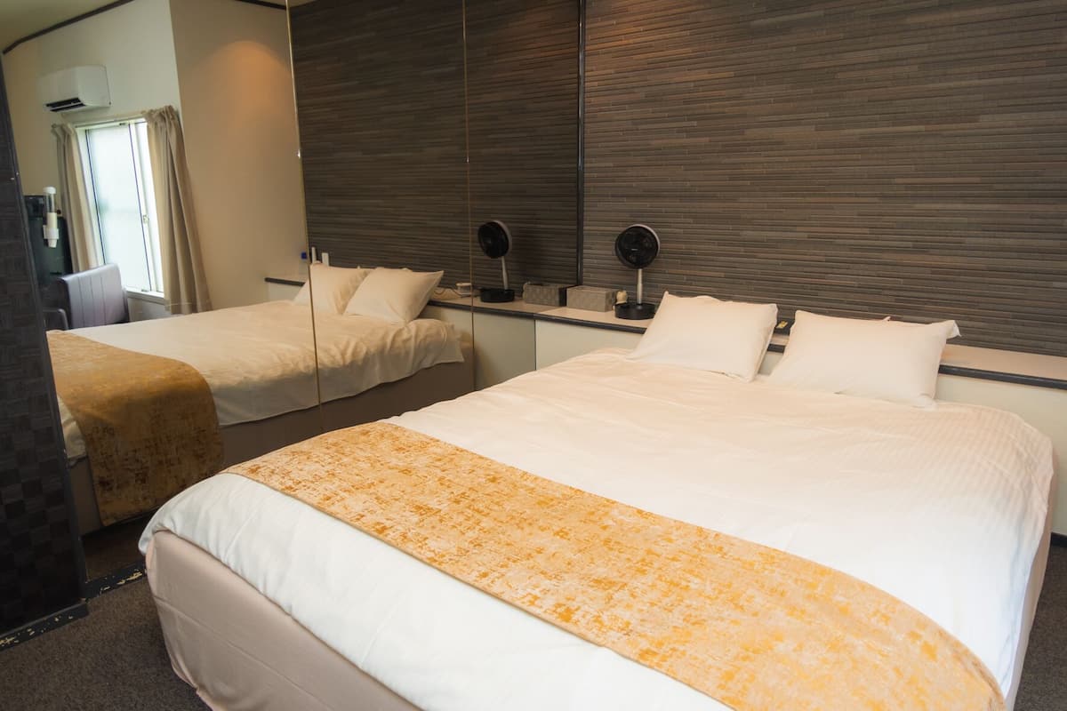 A hotel room with two beds, a large mirror, a window with curtains, and a wall-mounted air conditioner.
