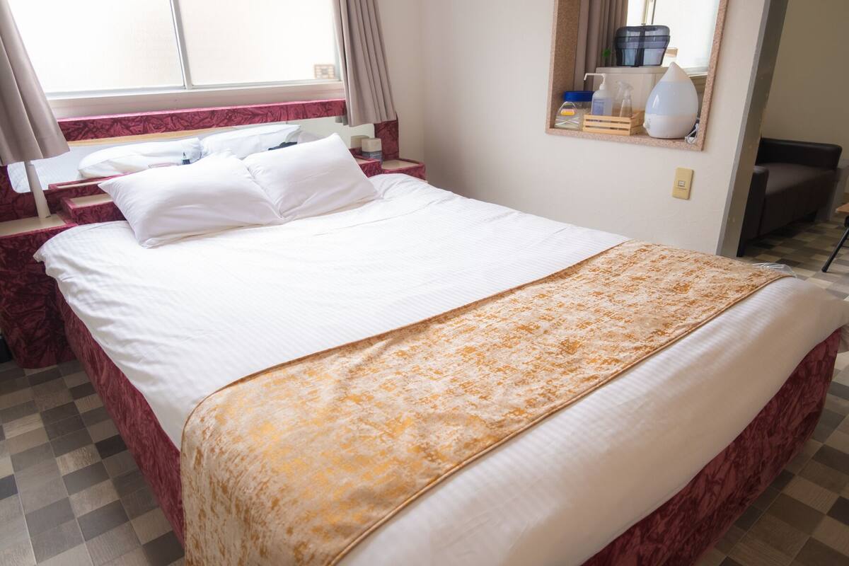 A hotel room with a bed, a bedside table, a mirror, and a window.