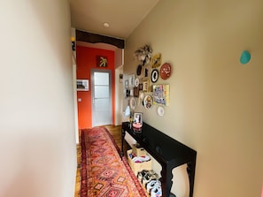 Um corredor com carpete estampado, um banco e diversas decorações nas paredes, incluindo quadros e um relógio.