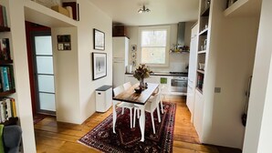 A modern kitchen with white cabinets, a wooden dining table, and a patterned rug.