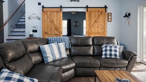 A modern living room with a dark leather sectional sofa, a wooden coffee table, and a large sliding barn door. - King Bed~Cedar soaking Hot Tub~5min walk to Beach~No Cleaning Fee (Two Rivers)
