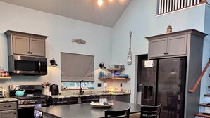 A modern kitchen with a central island, stainless steel appliances, and a staircase with a railing. - King Bed~Cedar soaking Hot Tub~5min walk to Beach~No Cleaning Fee (Two Rivers)