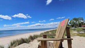 A wooden beach chair with a pink design on the backrest, positioned on a sandy beach with a clear blue sky and a calm sea in the background. - King Bed~Cedar soaking Hot Tub~5min walk to Beach~No Cleaning Fee (Two Rivers)
