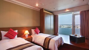 A hotel room with two beds, a nightstand with a lamp, a small table, and a large window offering a city view. - apvc-resort (Lukang)